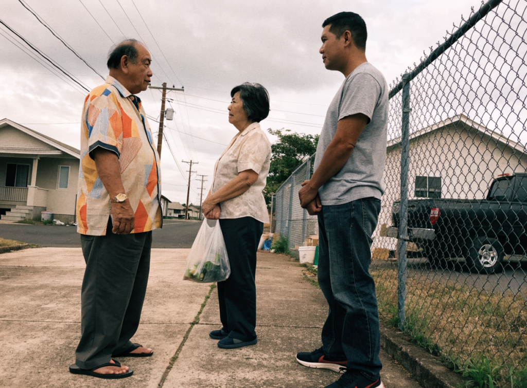 Three neighbors talk story at the end of a driveway on an Oahu street